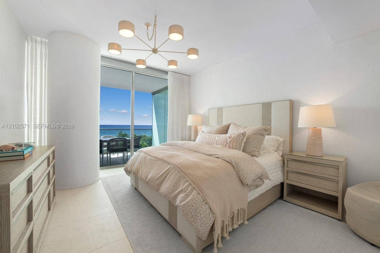 10201 Collins Avenue, #502, Bal Harbour, FL 33154 Floor-to-ceiling glass sliding doors with access to an exterior terrace, neutral stone-finish flooring, and a contemporary multi-arm chandelier