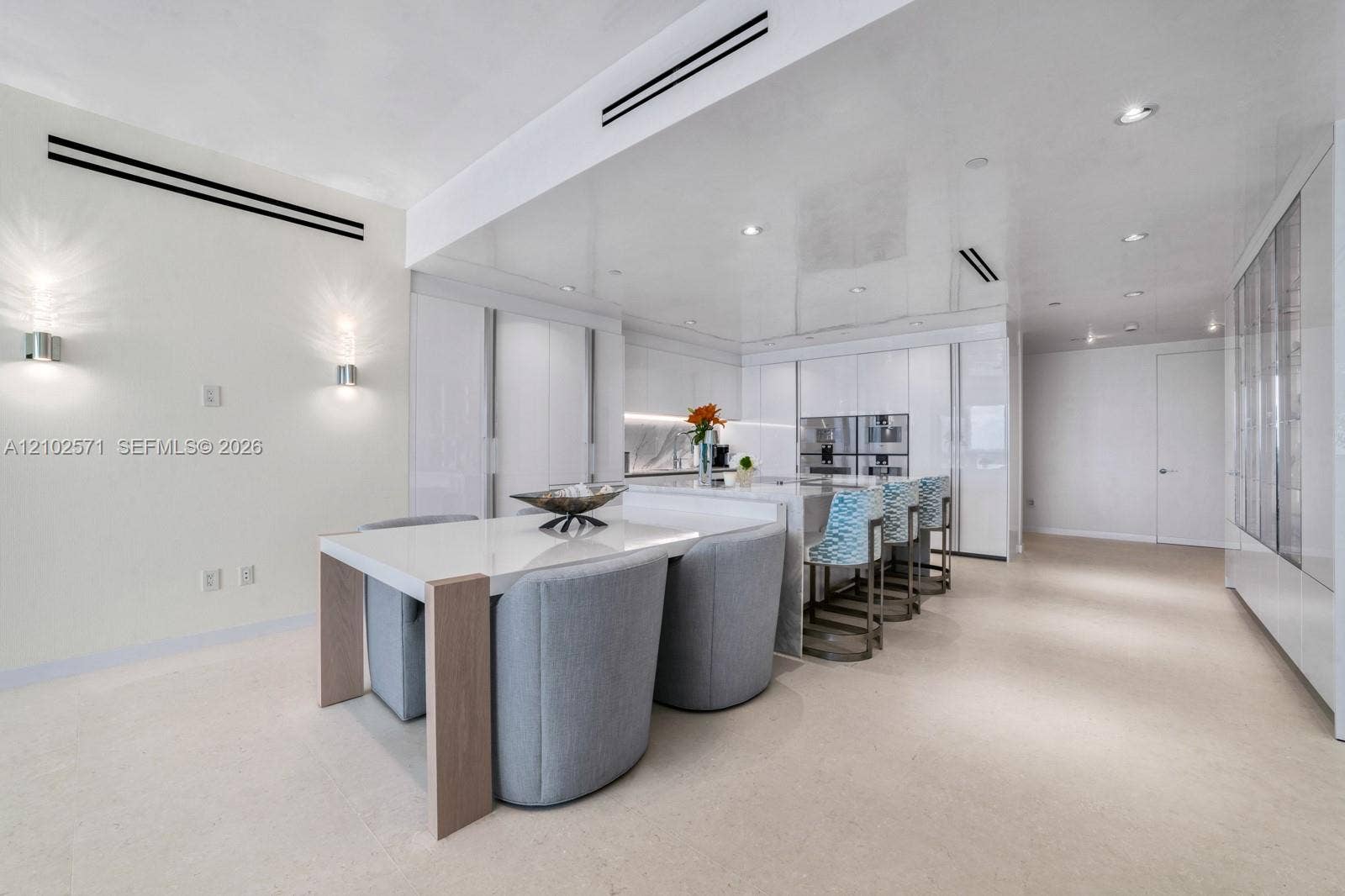 10201 Collins Avenue, #502, Bal Harbour, FL 33154 Modern kitchen featuring a central island with a stone countertop, integrated high-end stainless steel appliances, seamless white cabinetry, recessed ceiling lighting, and linear wall sconces