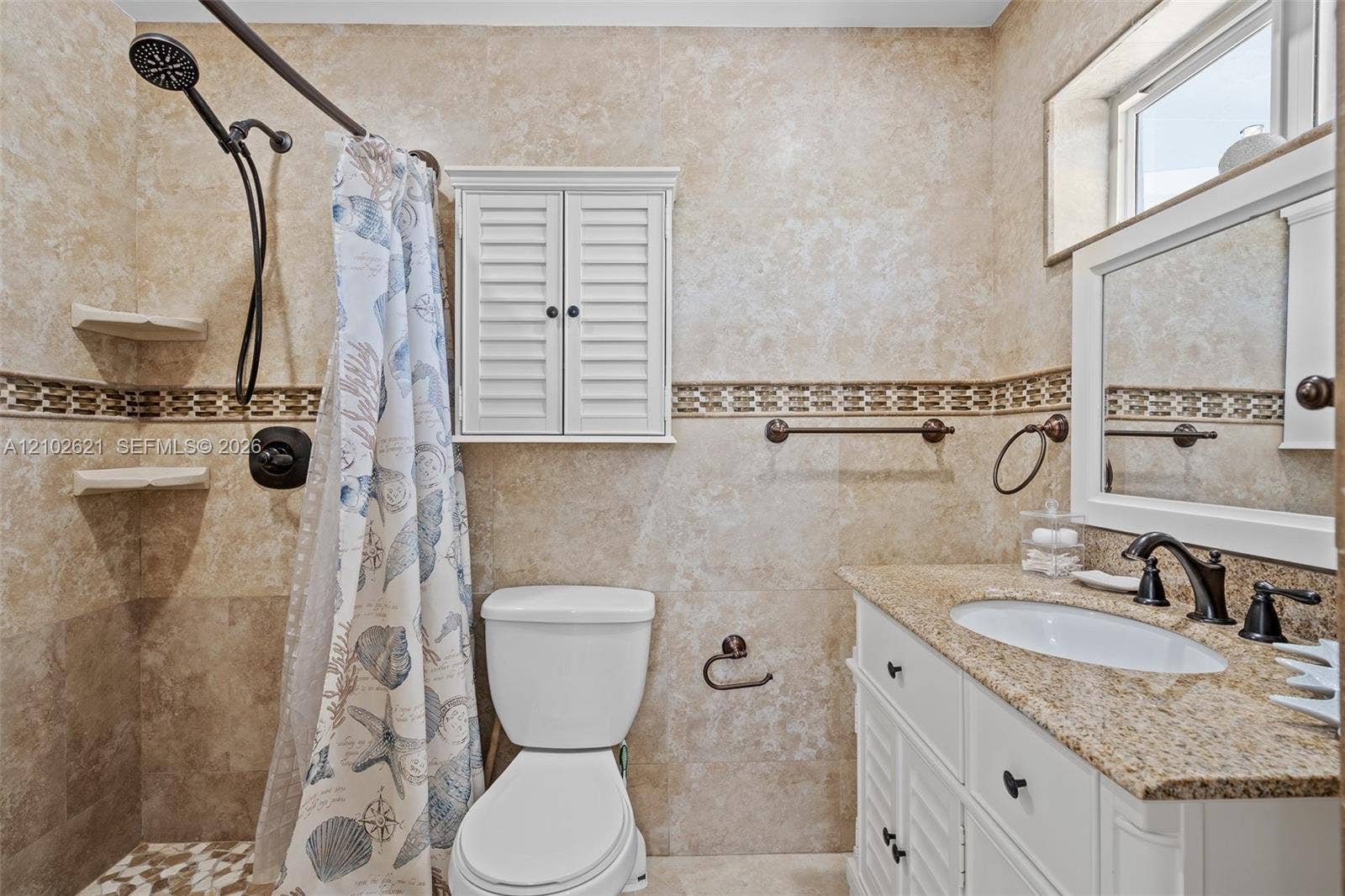Tiled shower with mosaic accent, white louvered vanity, granite countertop, undermount sink, and transom window
