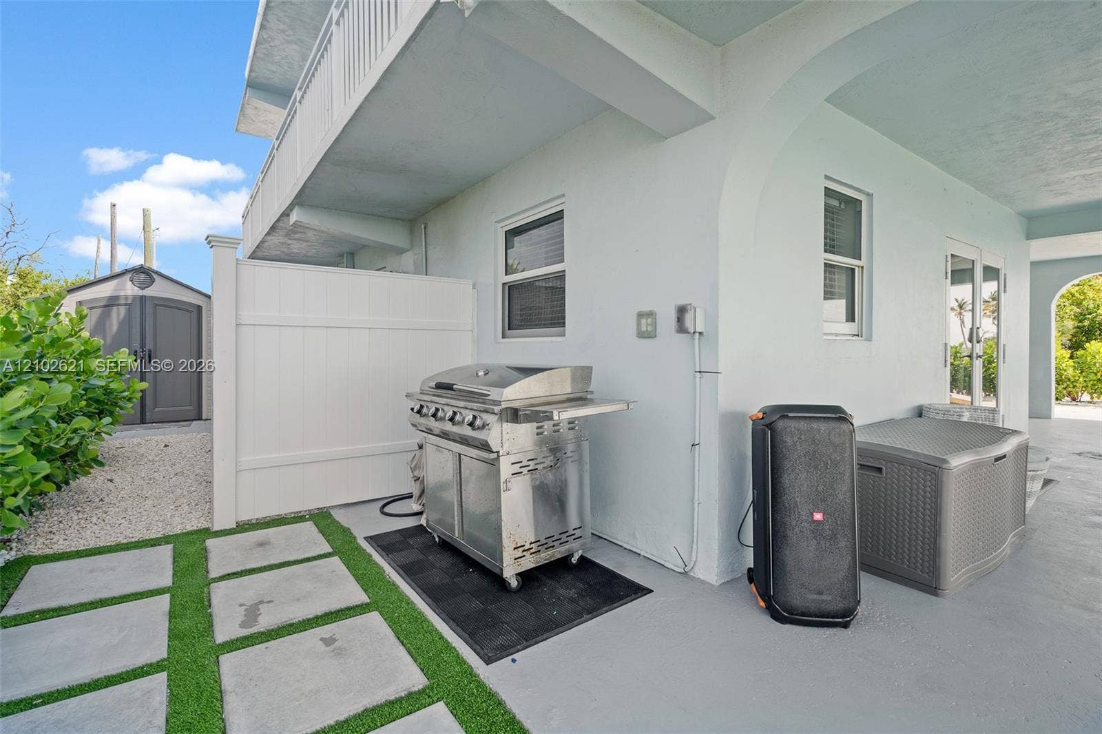 Covered patio area with concrete flooring, framed by arched entryways, featuring a white privacy fence and a built-in outdoor storage shed