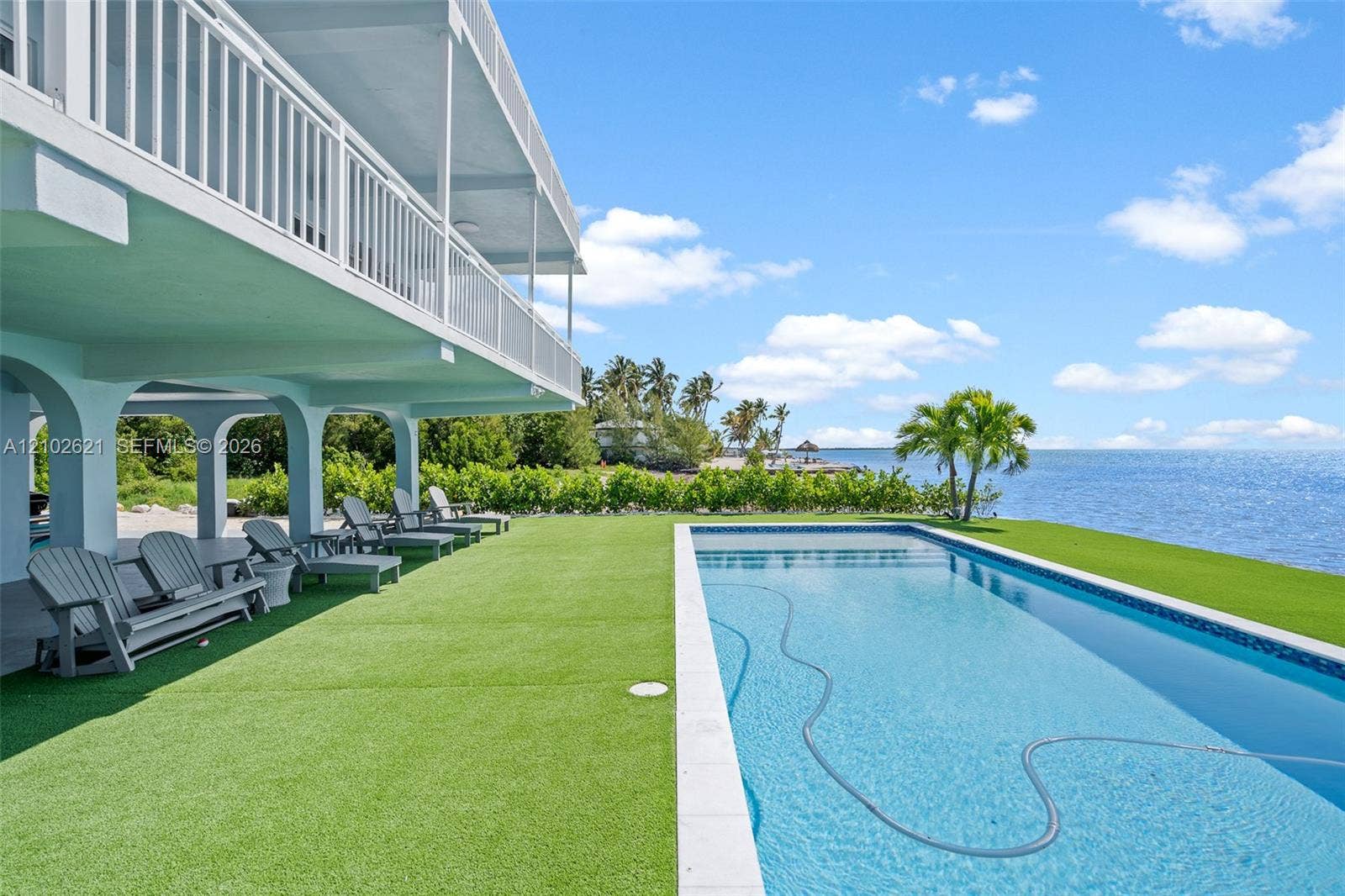 Waterfront property featuring a large swimming pool, expansive artificial turf lawn, and an elevated balcony with white railings