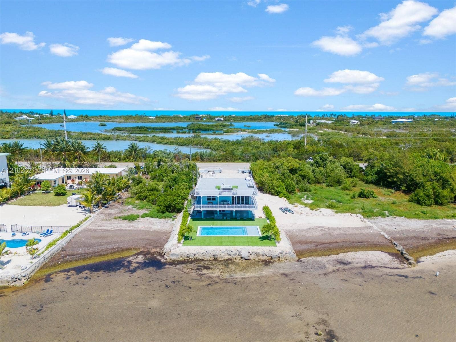 Modern waterfront residence featuring a blue-tiled swimming pool and a surrounding artificial turf patio