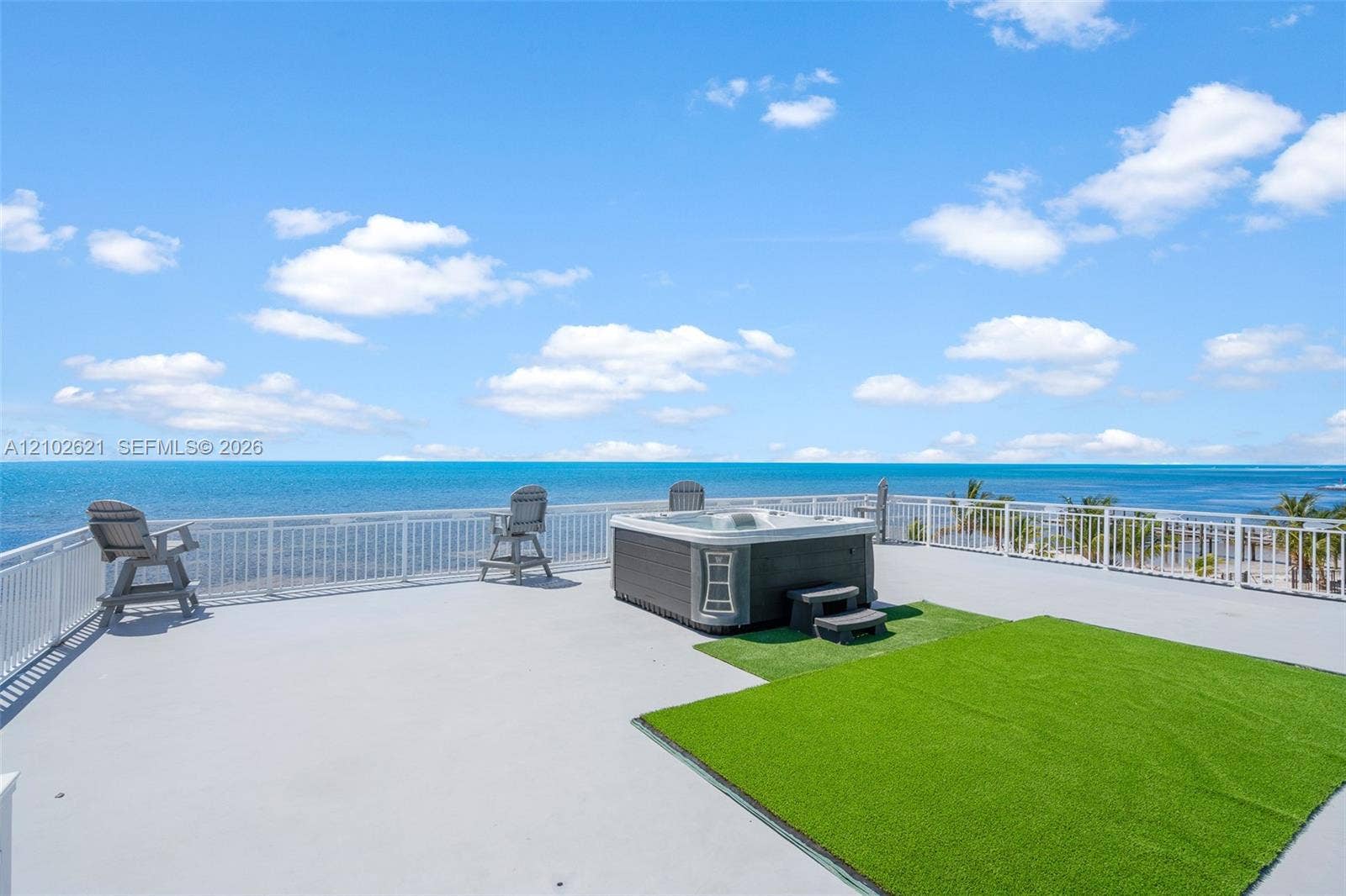 Rooftop deck featuring a hot tub, artificial turf area, and white perimeter railing