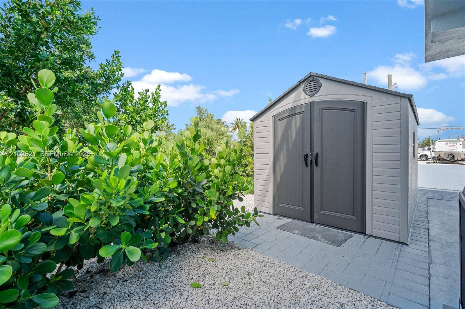 Storage shed with double doors, paved walkway, and lush perimeter landscaping