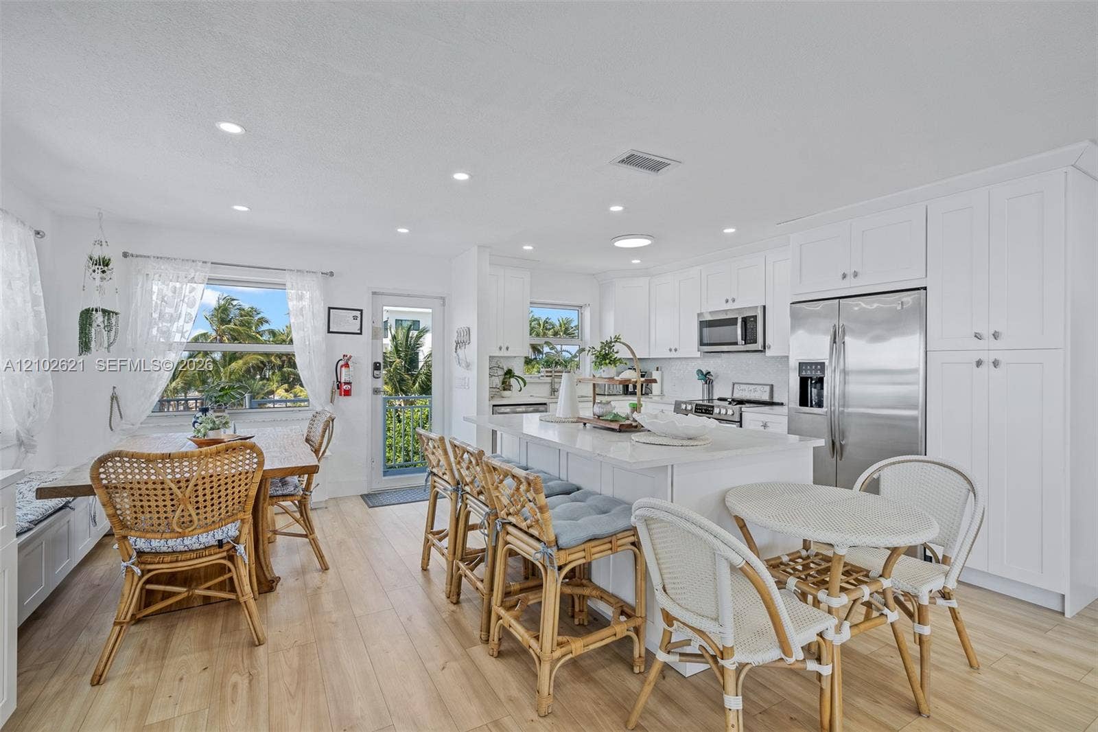 White shaker cabinetry, stainless steel appliances, recessed lighting, wood-finish flooring, and a center island with countertop seating