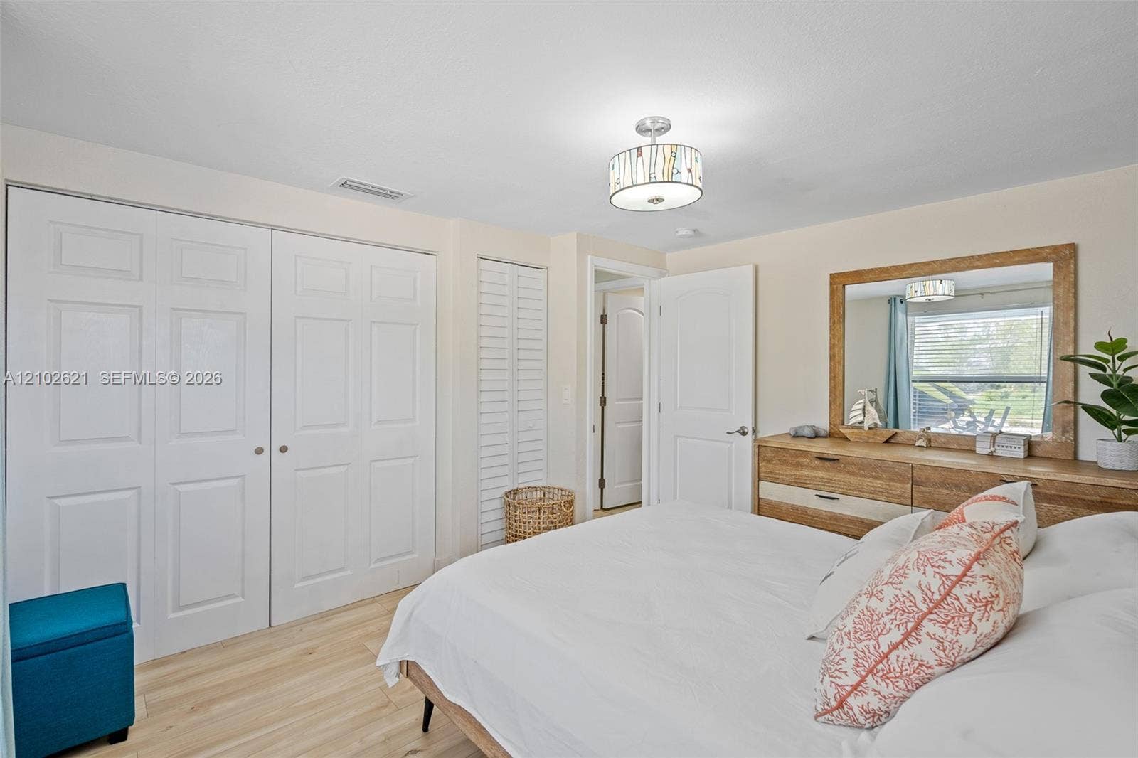 Light wood-finish flooring, two sets of bi-fold closet doors, a contemporary ceiling light fixture, and a built-in dresser with a framed mirror