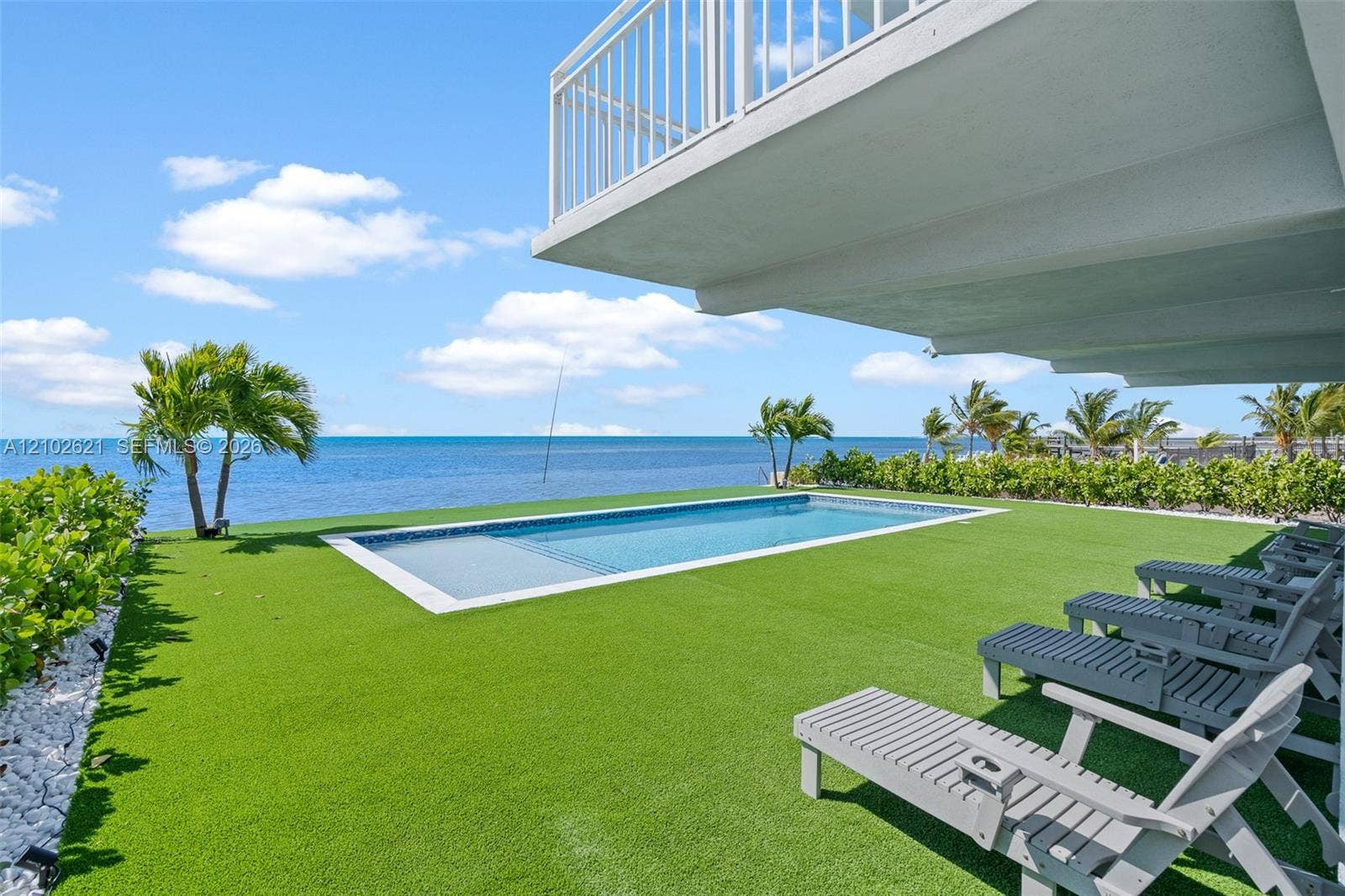 In-ground swimming pool with a tile border, artificial turf lawn, and direct waterfront access
