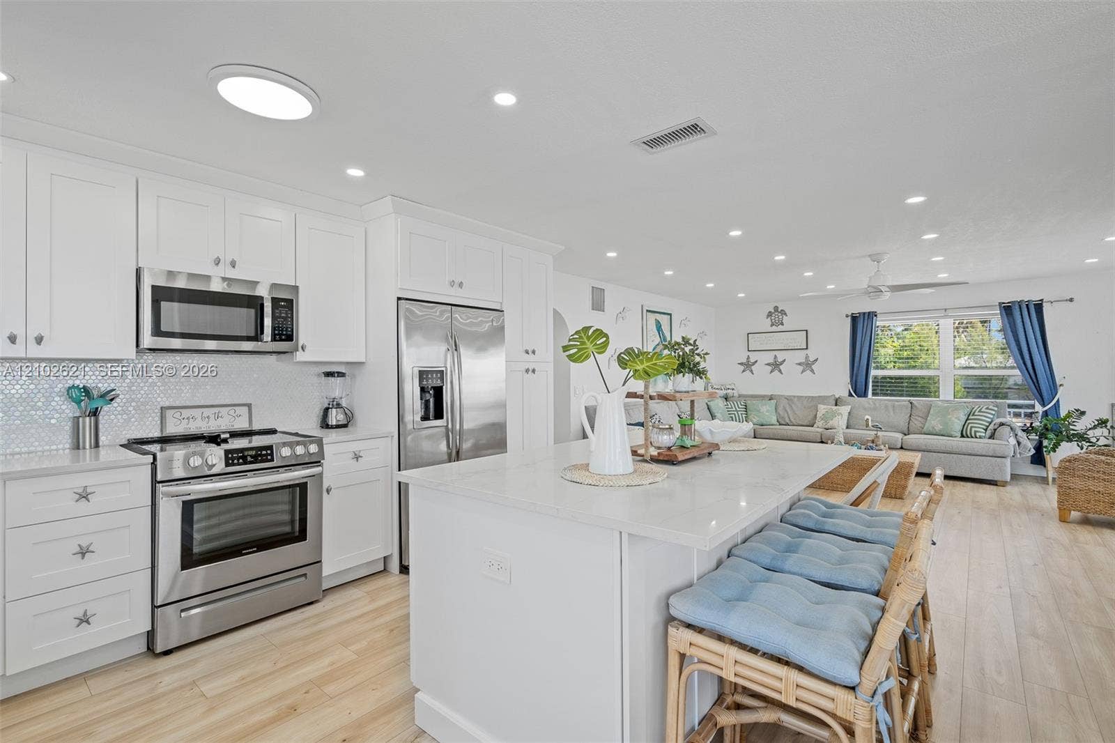 Kitchen featuring white shaker cabinetry, stainless steel appliances, a white island, light-toned wood-finish flooring, and recessed lighting