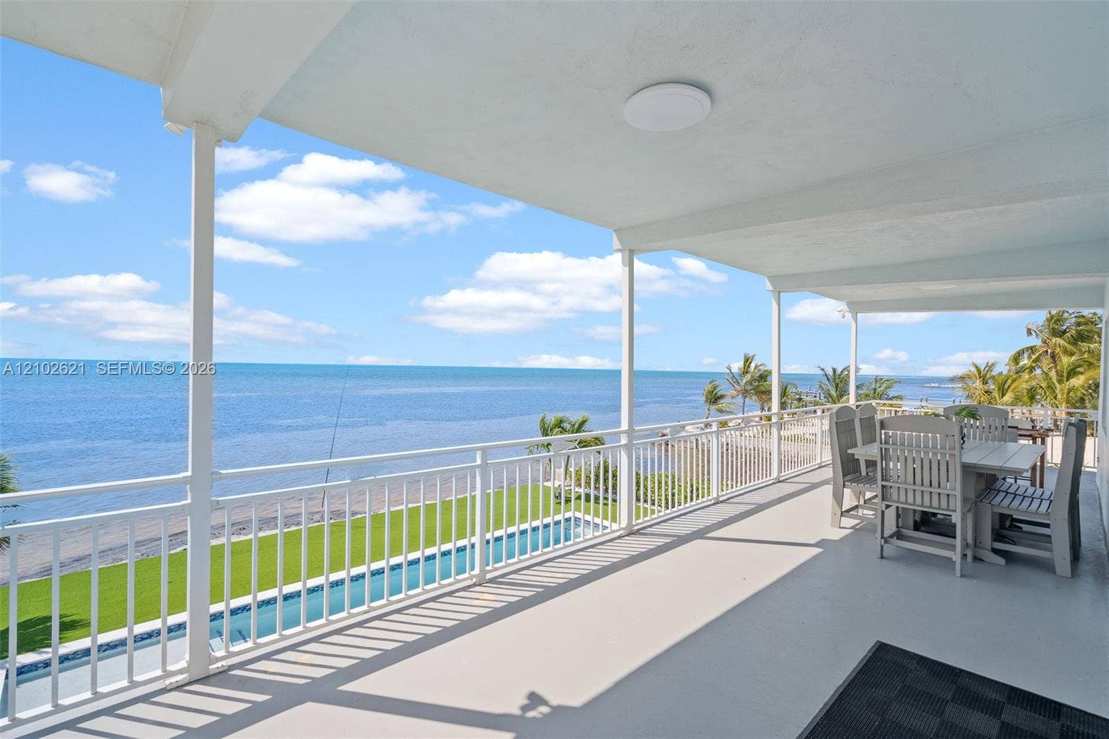 Expansive covered balcony featuring a coastal backdrop, white railing, outdoor ceiling light, and direct water exposure