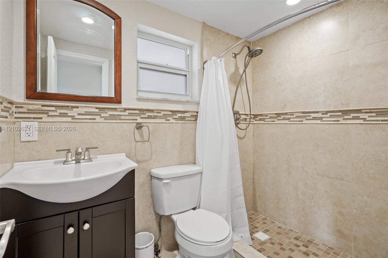 Bathroom featuring a dark wood-finish vanity with an integrated sink, a walk-in shower with mosaic tile flooring, and beige tiled walls with a decorative mosaic accent band