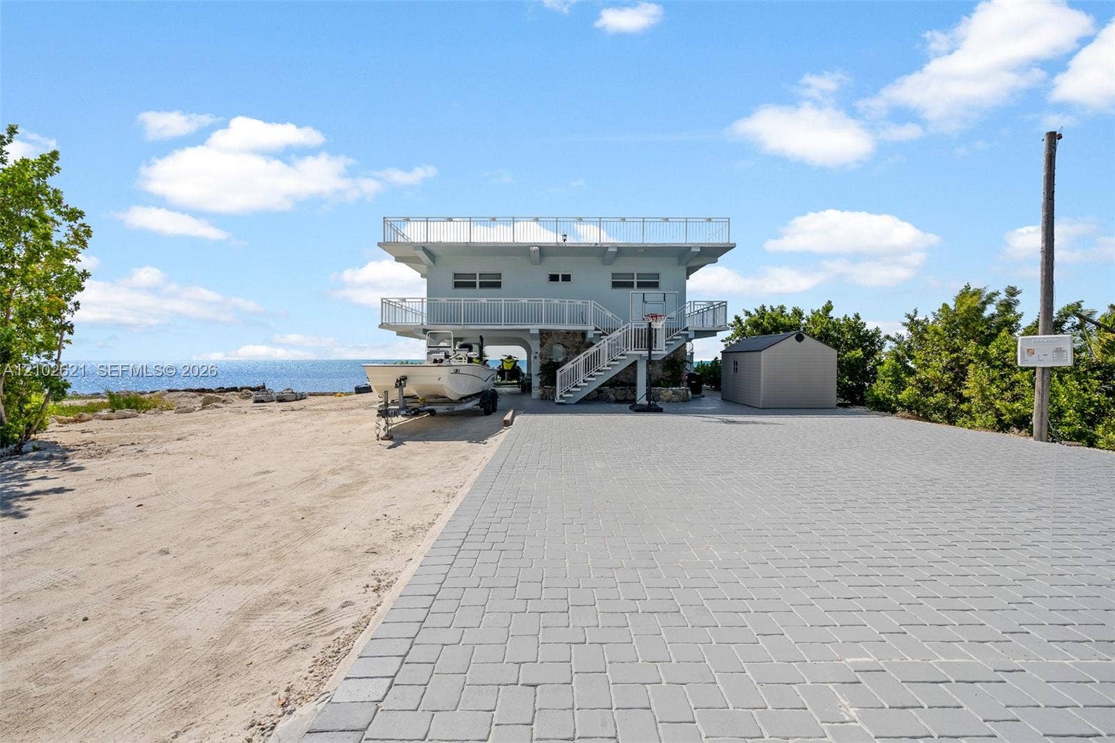 Two-story coastal structure with multiple balconies, a rooftop deck, and an exterior staircase