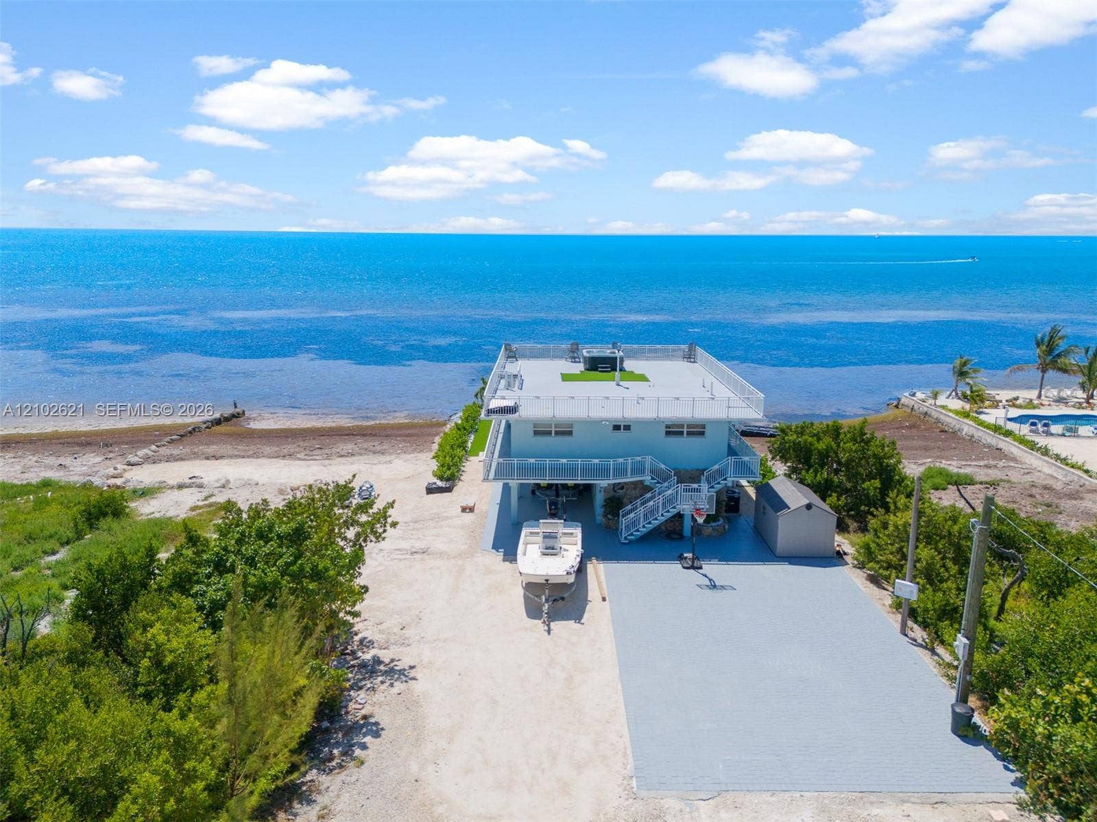 Waterfront property featuring a flat roofline, elevated construction, a paved court, and a storage shed