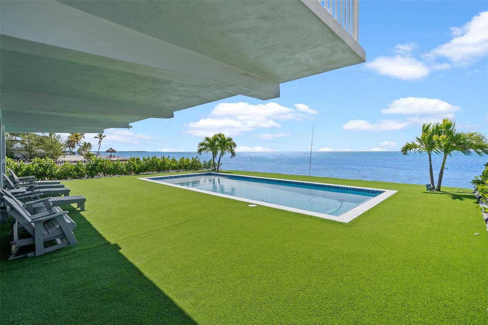 Lush artificial turf surrounds a rectangular swimming pool, bordered by tropical landscaping