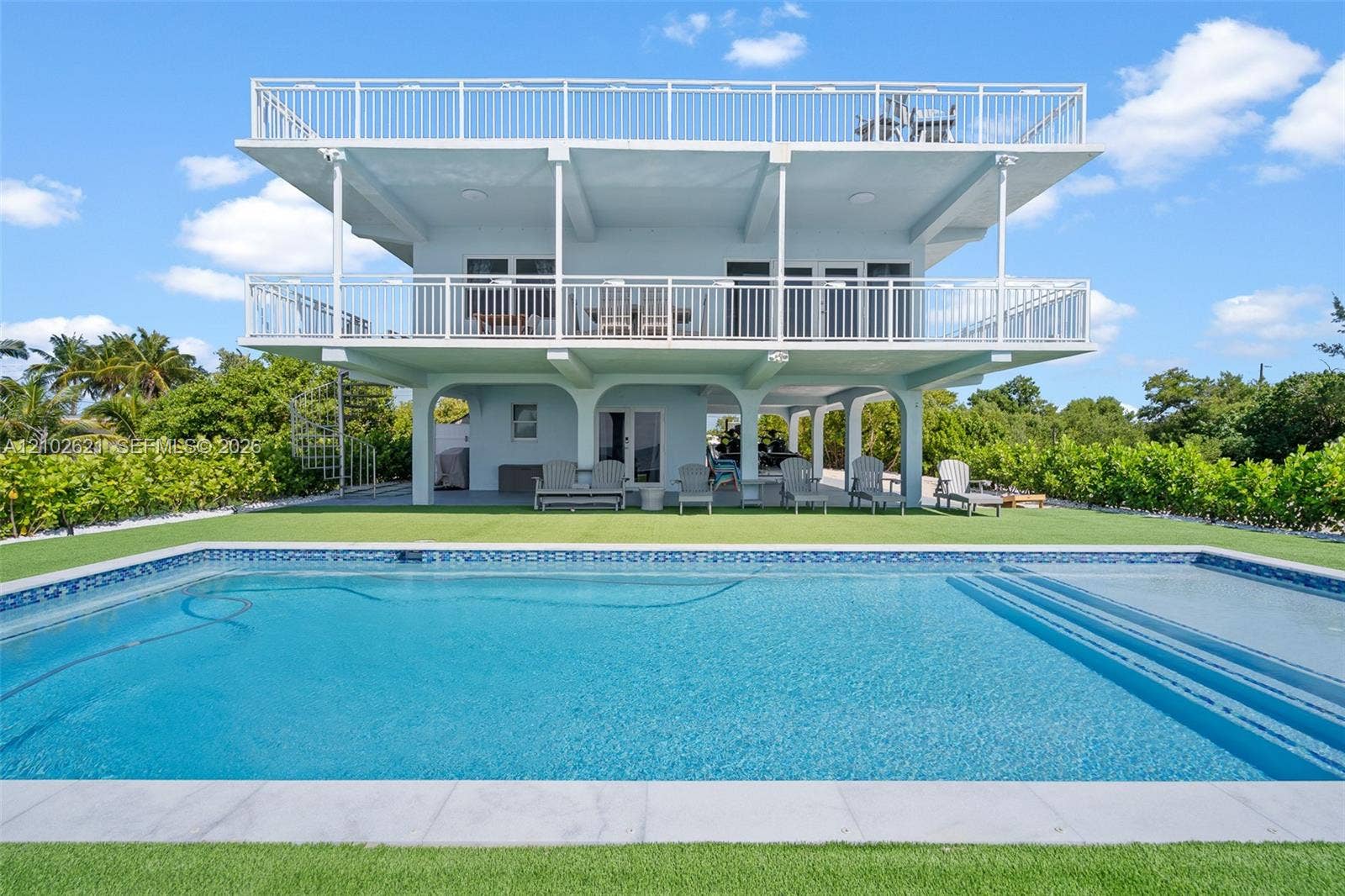 Multi-level exterior with multiple balconies, an expansive swimming pool with tiled coping, and an artificial turf surround