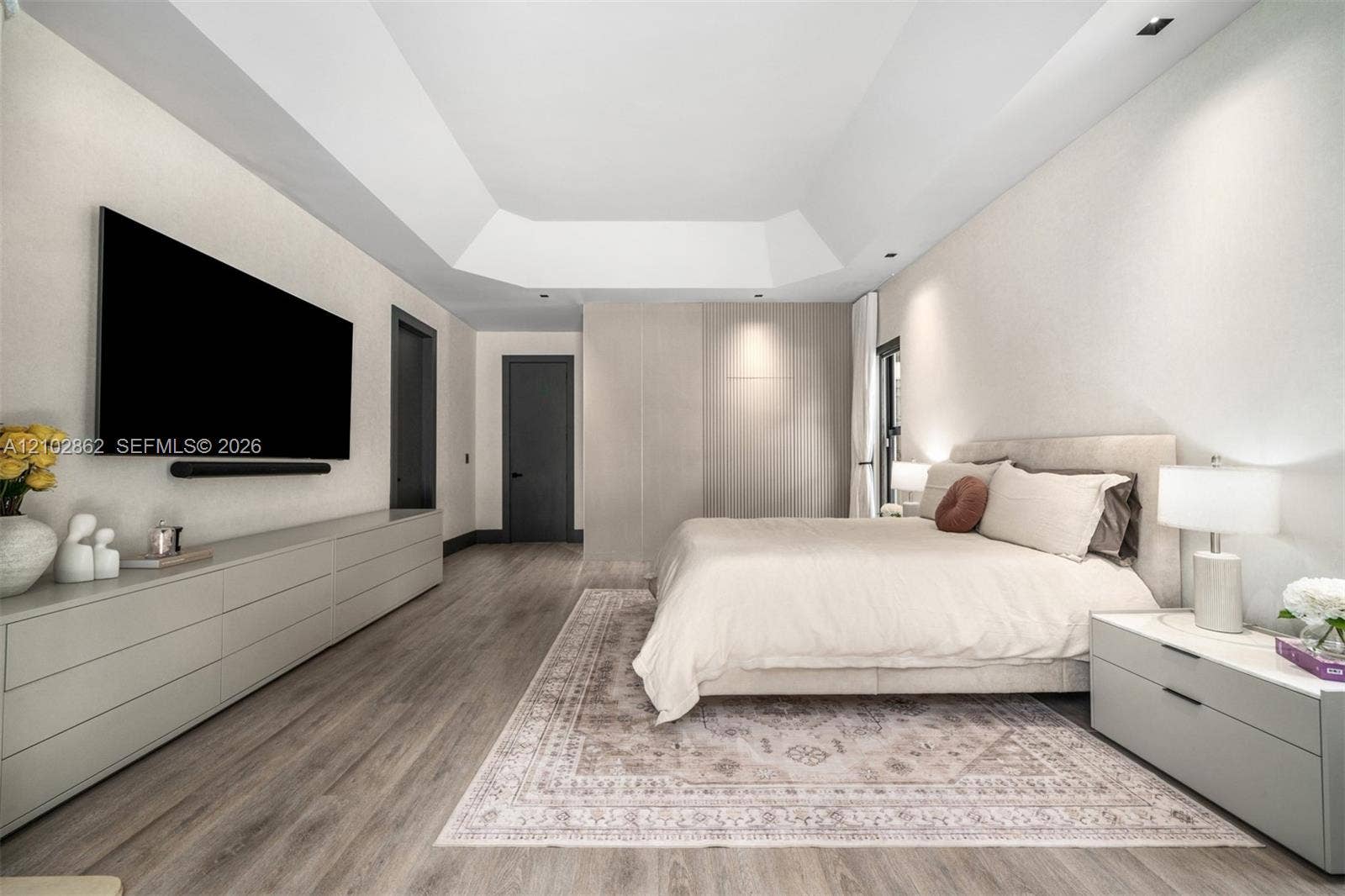 Tray ceiling with recessed lighting, integrated floor-to-ceiling cabinetry, wood-finish flooring, and minimalist flat-panel doors