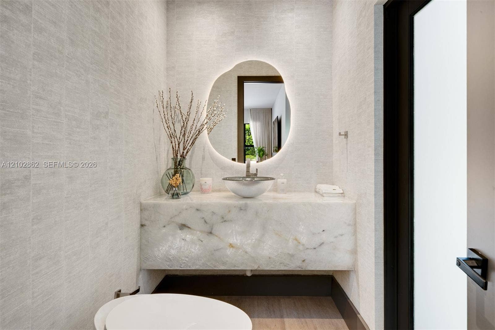 Floating stone vanity with a vessel sink, integrated LED-backlit organic-shaped mirror, and textured wall finish