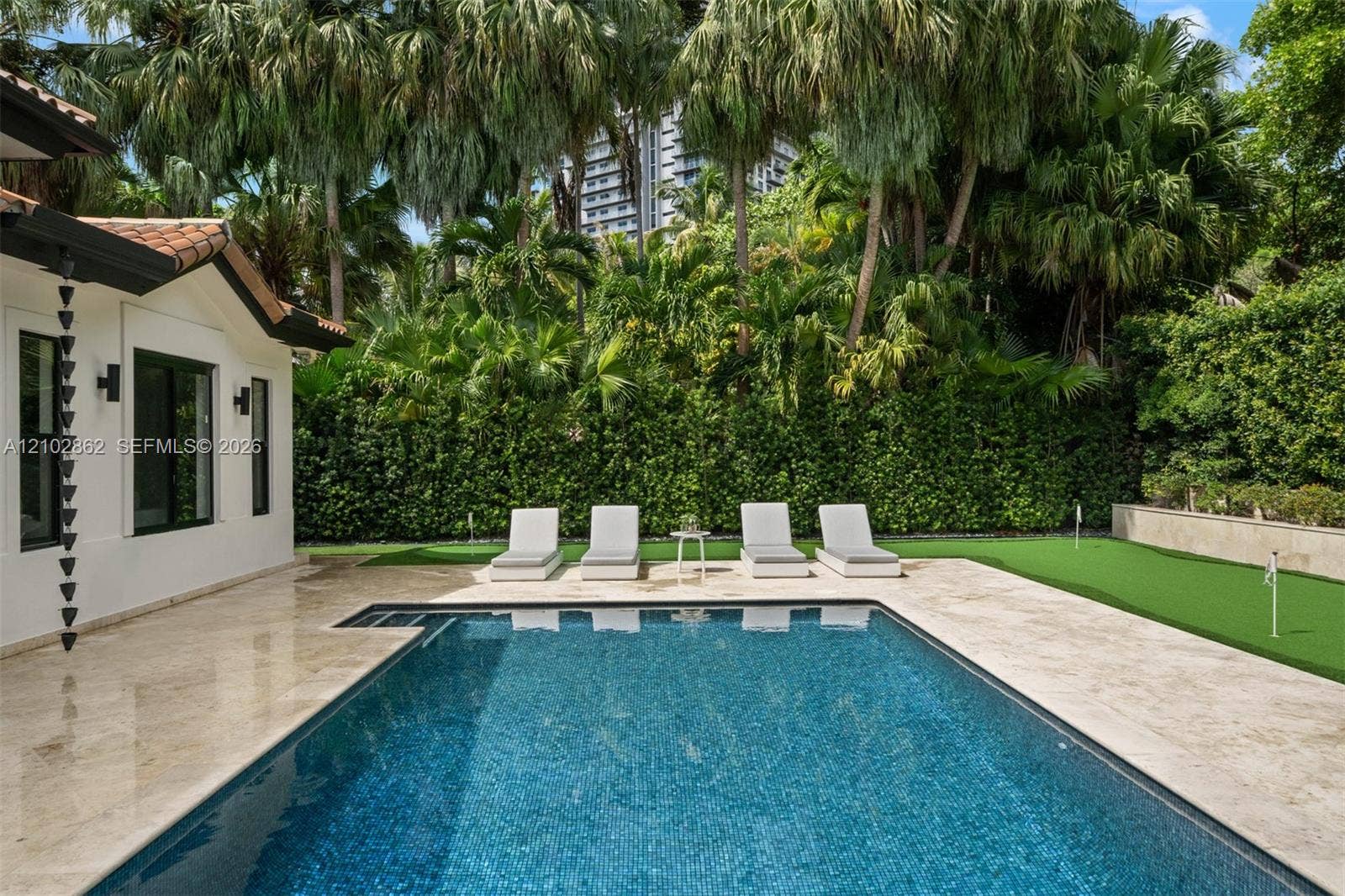 Outdoor pool with stone-tiled decking, integrated putting green, and perimeter privacy hedges