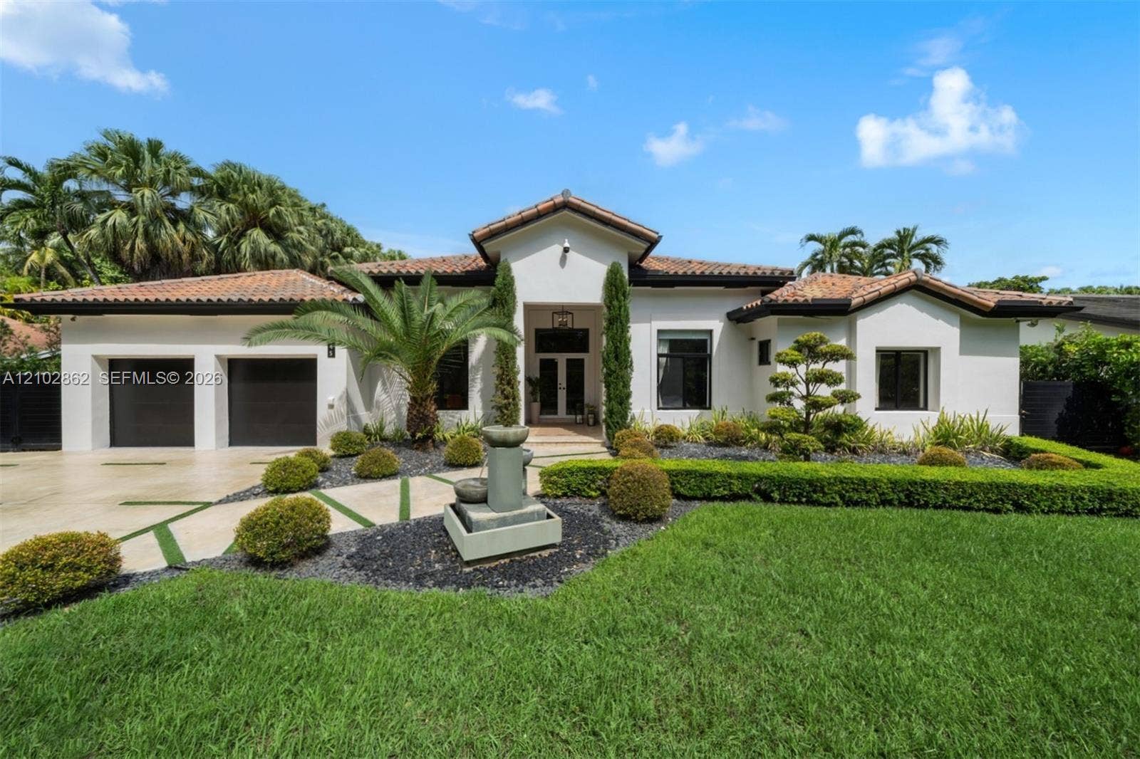 Single-story residence featuring a tile roof, stucco exterior, two-car garage, stone water fountain, and manicured landscaping