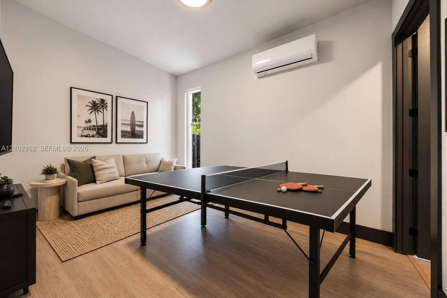 Room featuring wood-finish flooring, wall-mounted ductless air conditioning unit, tall vertical window, and high-contrast dark door casing