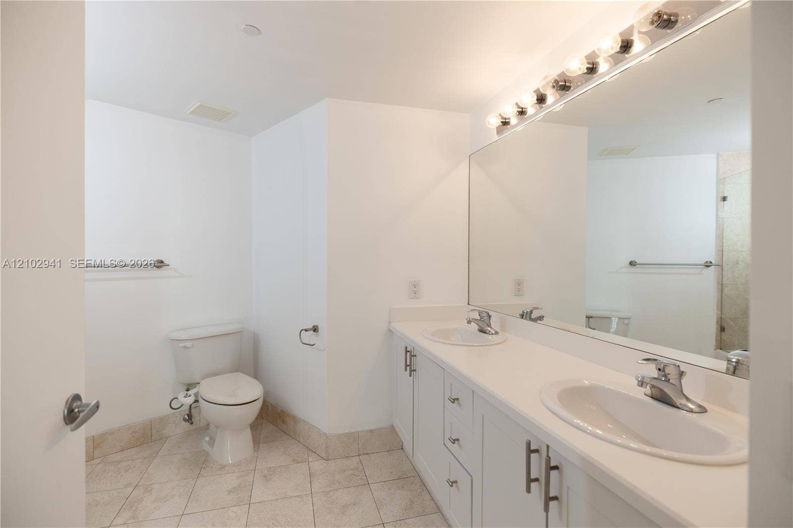 2475 Brickell Avenue, #1807, Miami, FL 33129 Bathroom featuring a dual-sink vanity with white cabinetry, light-toned countertops, a full-width wall mirror, and neutral-toned tile flooring