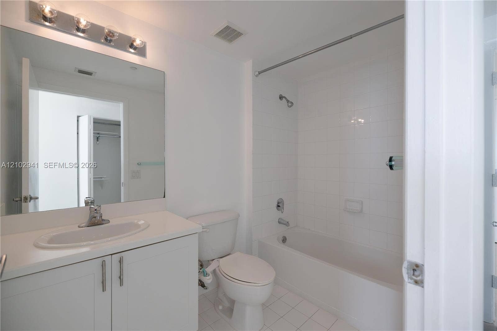 2475 Brickell Avenue, #1807, Miami, FL 33129 Bathroom featuring a vanity with an integrated oval sink, countertop, oversized wall mirror, four-light vanity fixture, and a tub-shower combination with white wall tile