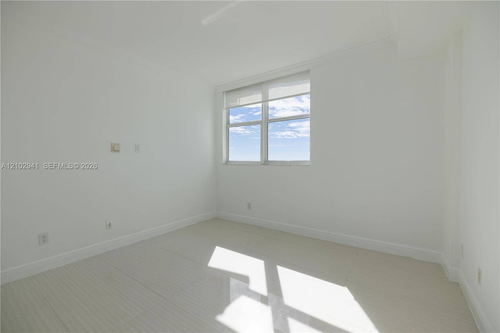 2475 Brickell Avenue, #1807, Miami, FL 33129 Neutral-toned interior space featuring light-colored tile flooring, smooth wall finishes, and a window with a retractable roller shade
