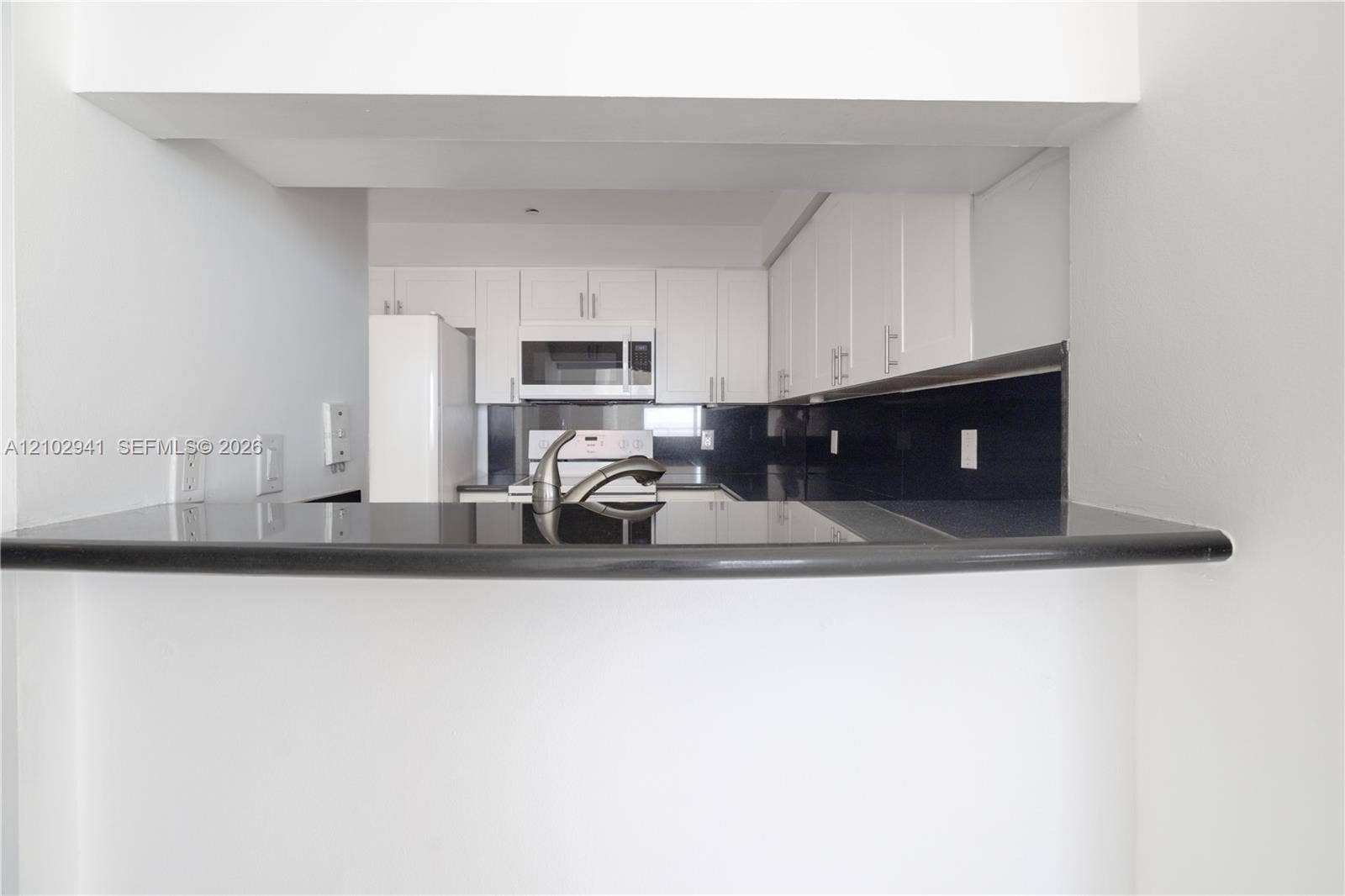 2475 Brickell Avenue, #1807, Miami, FL 33129 Kitchen featuring white cabinetry, contrasting dark countertops, a dark backsplash, a built-in microwave, and a stainless steel faucet