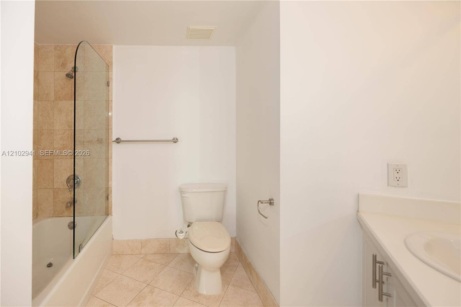 2475 Brickell Avenue, #1807, Miami, FL 33129 Bathroom featuring a tub-shower combination with a glass panel, stone-finish tile surround and flooring, and a solid-surface vanity countertop