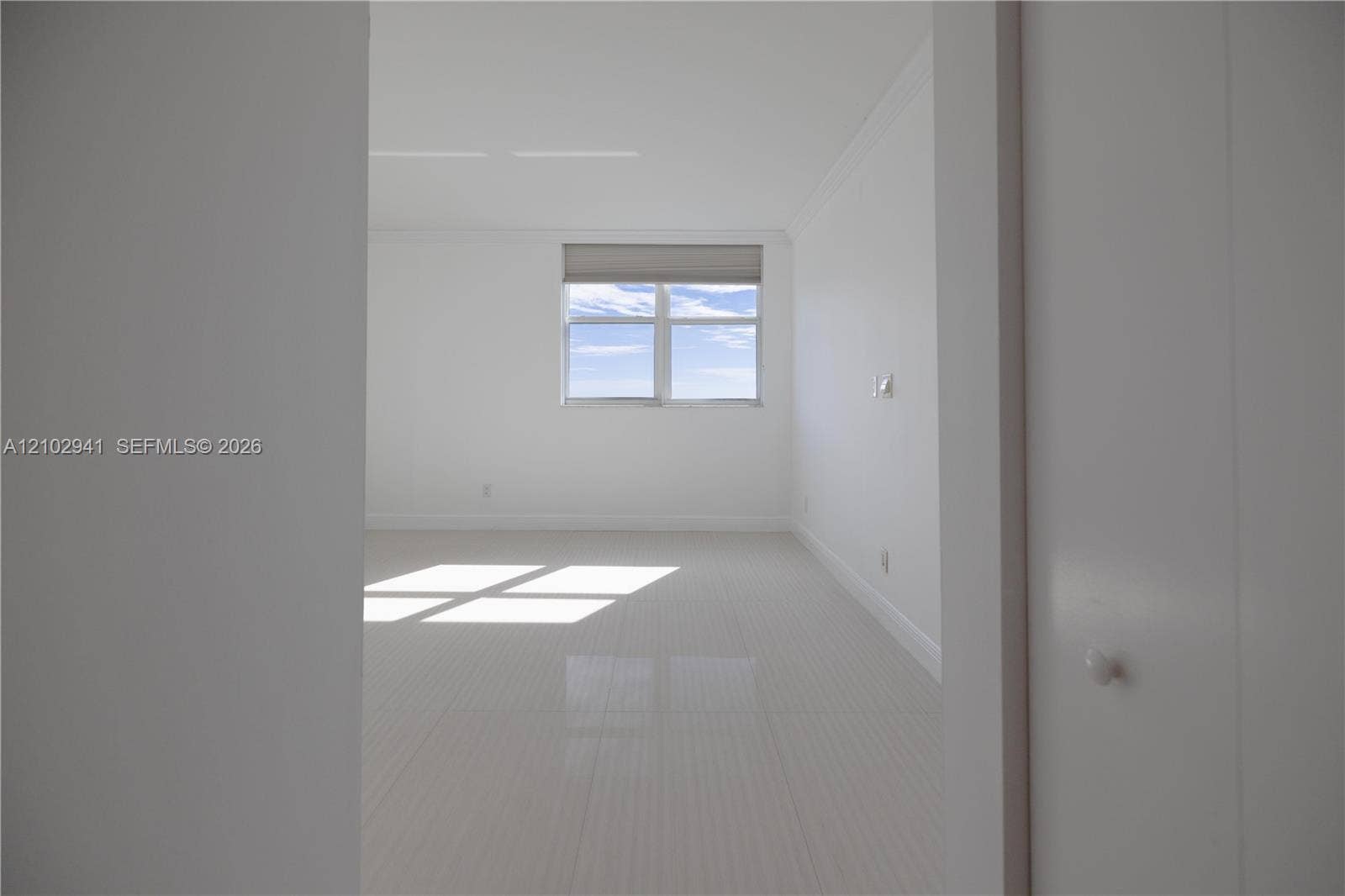 2475 Brickell Avenue, #1807, Miami, FL 33129 Neutral interior featuring large-format polished tile flooring, crisp white walls, crown molding, and a dual-pane window