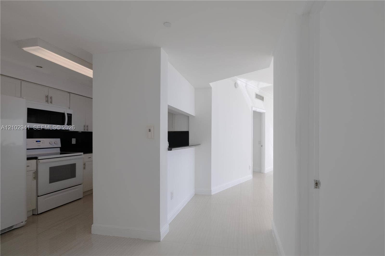 2475 Brickell Avenue, #1807, Miami, FL 33129 Kitchen featuring flat-panel white cabinetry, a black backsplash, integrated microwave, and a pass-through opening with a ledge