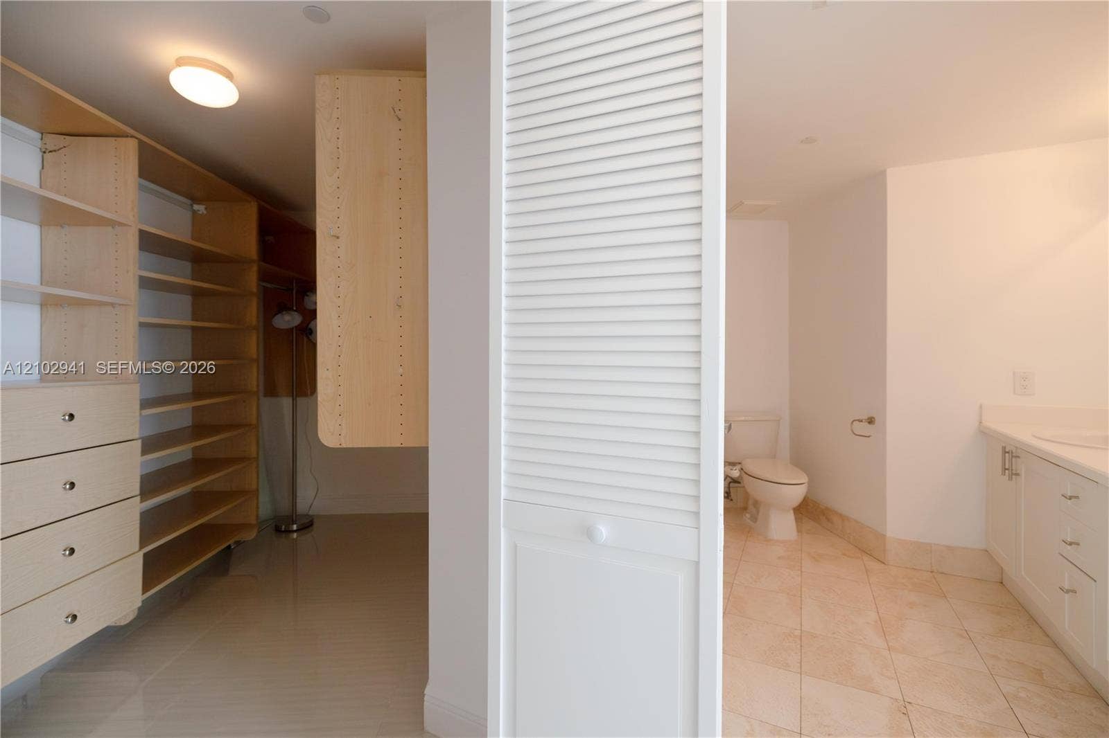 2475 Brickell Avenue, #1807, Miami, FL 33129 Custom built-in wood shelving and cabinetry with integrated drawers, light-toned tile flooring, white louvered closet doors, and a vanity featuring neutral cabinetry