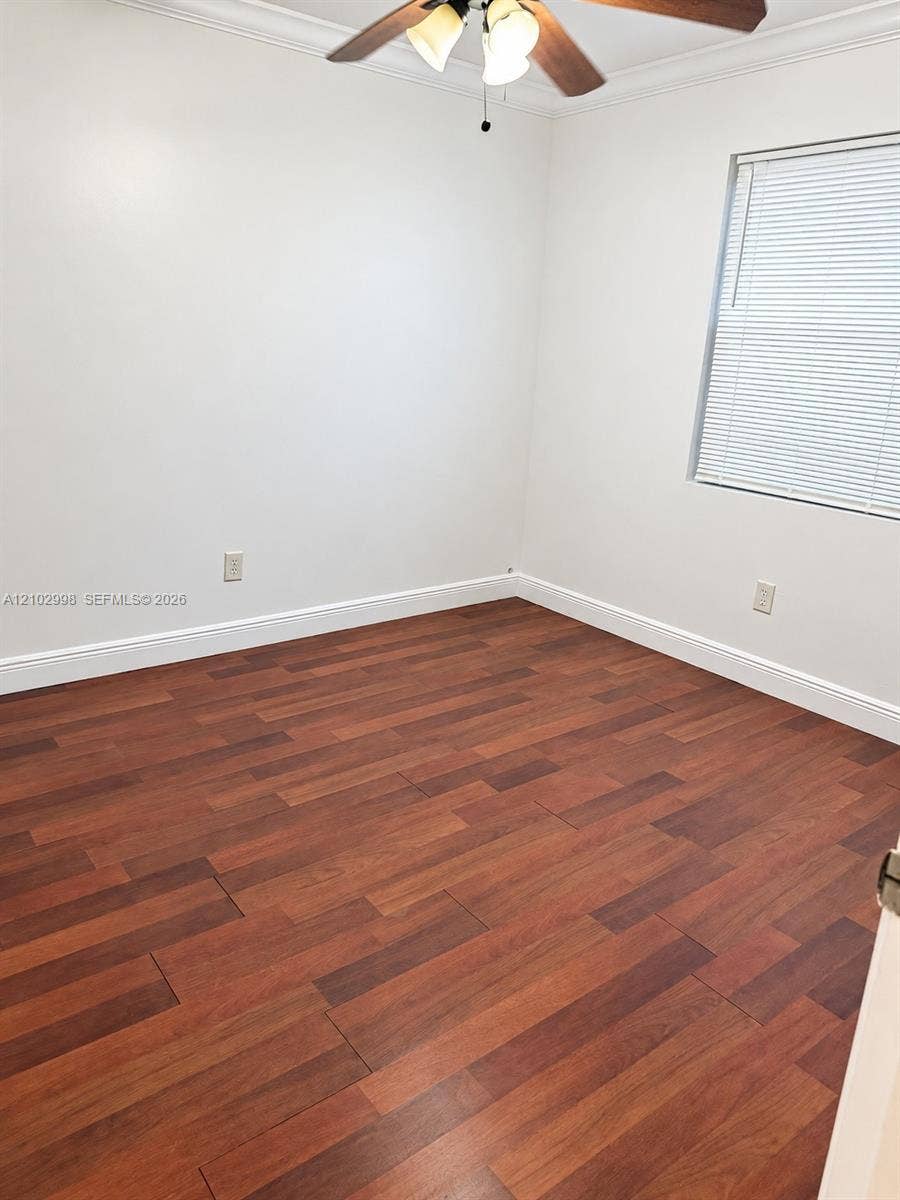 Interior space featuring wood-finish flooring, white walls, crown molding, and a ceiling fan with integrated lighting