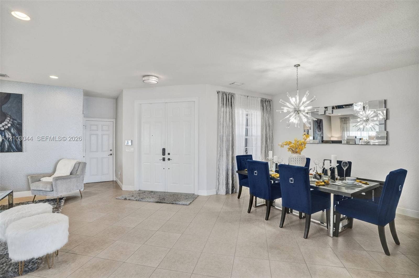 Open-concept space featuring neutral large-format tile flooring, recessed ceiling lighting, a contemporary multi-point starburst chandelier, and double-door entry