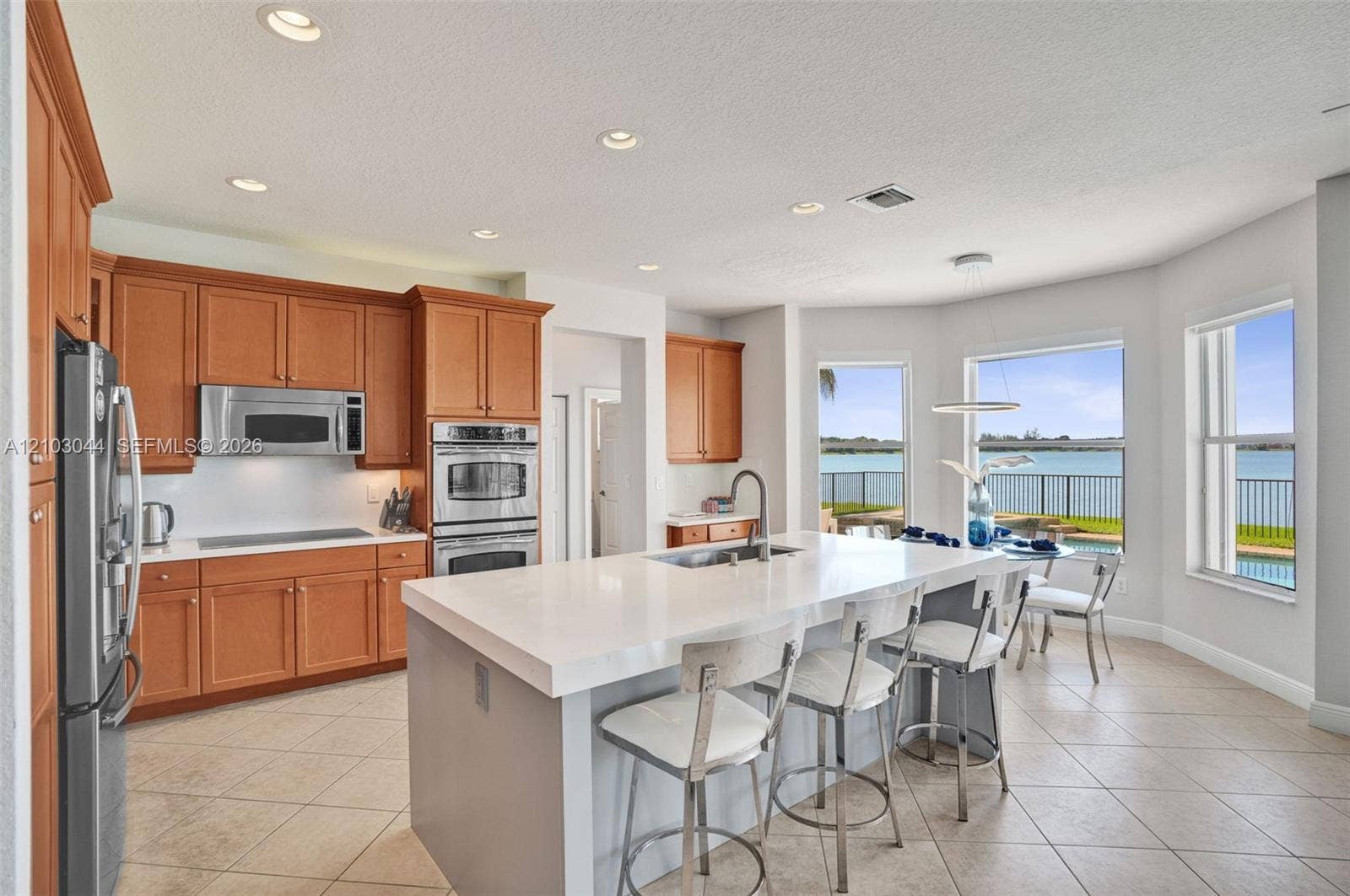 Kitchen featuring shaker-style cabinetry, quartz countertops, a central island with an integrated sink, built-in stainless steel double ovens, and water-facing windows
