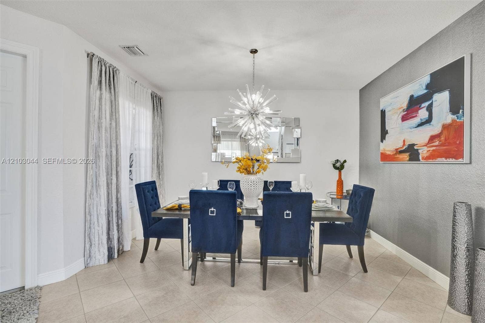 Dining space featuring oversized ceramic tile flooring, a neutral color palette with a grey accent wall, and a multi-spoke sunburst-style overhead light fixture