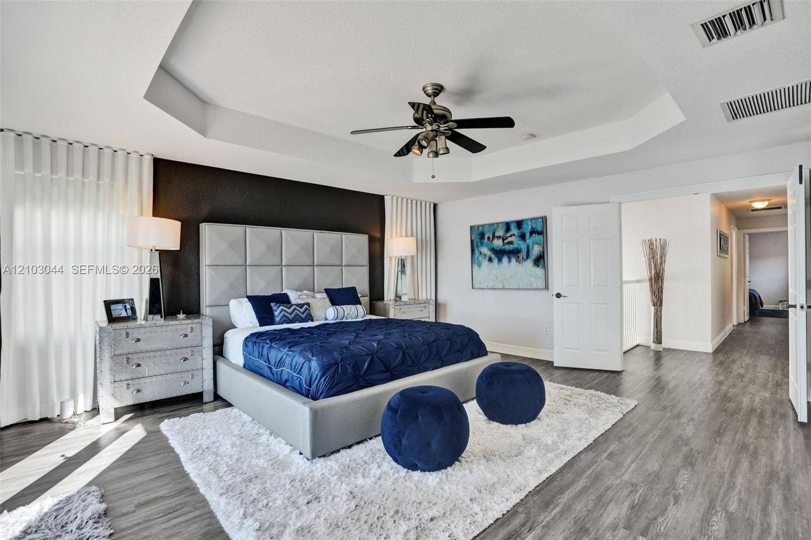 Spacious room featuring a recessed tray ceiling, wood-finish flooring, and a dramatic dark accent wall