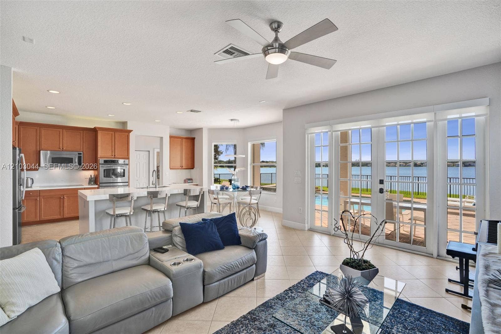 Open-concept living space featuring wood-finish cabinetry, a waterfall-edge center island with a built-in sink, recessed lighting, a modern ceiling fan, and sliding glass doors with exterior patio access