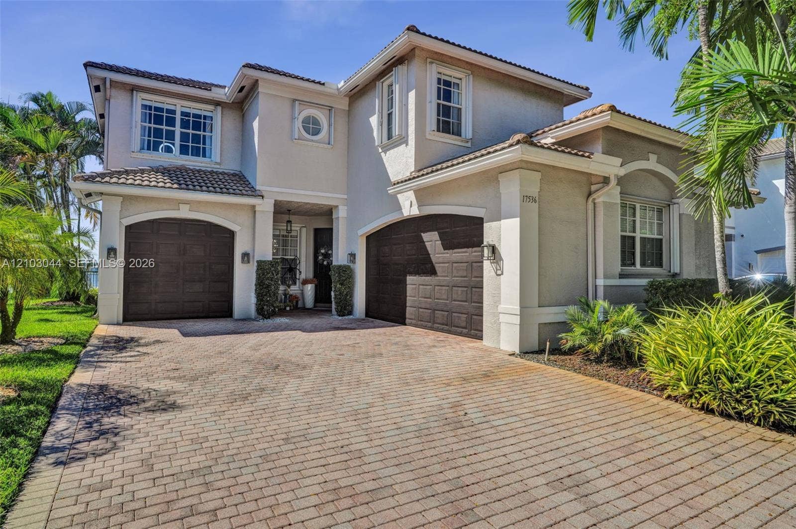 Two-story exterior featuring a paver driveway, multi-pane windows, arched garage openings, and a tile roof