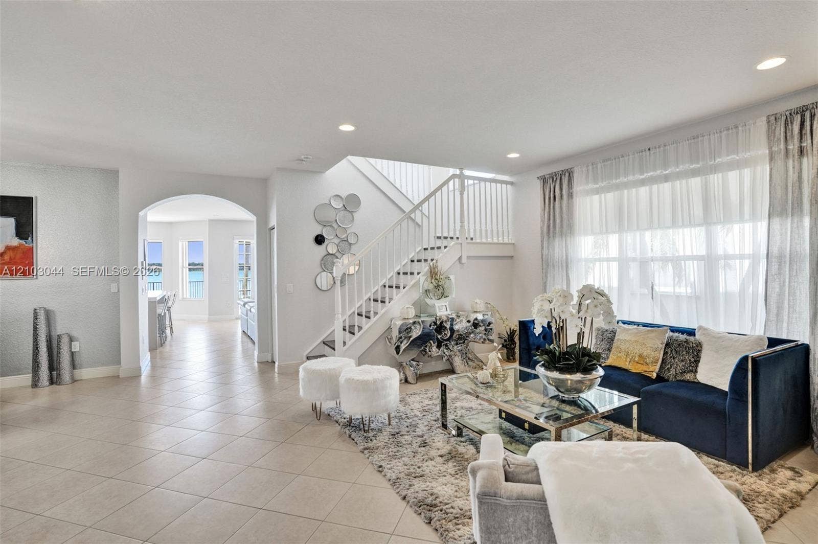 Open-concept floor plan featuring tile flooring, a prominent staircase with white balusters, an arched architectural entryway, and large windows with recessed lighting