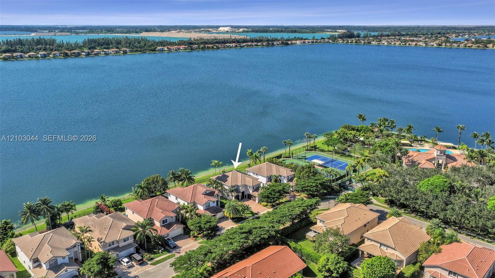 Aerial perspective of waterfront property featuring extensive shoreline access, tile roof construction, and proximity to community-maintained tennis courts
