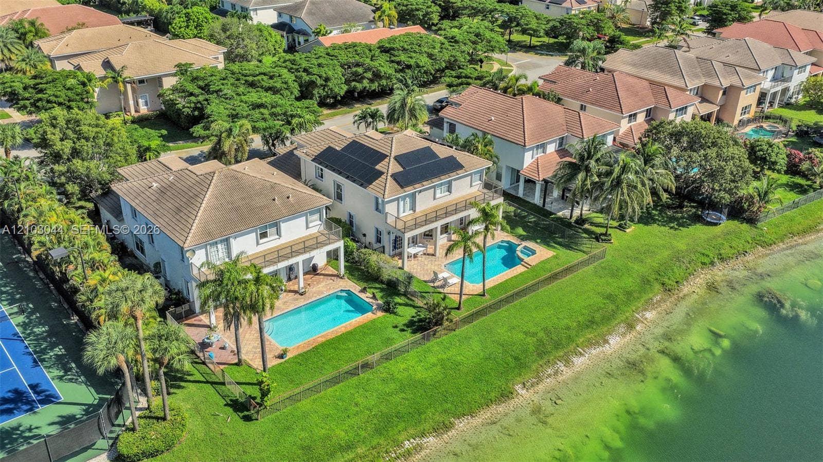 Aerial perspective of waterfront properties featuring tiled roofs, integrated solar panels, paved pool decks, and private swimming pools