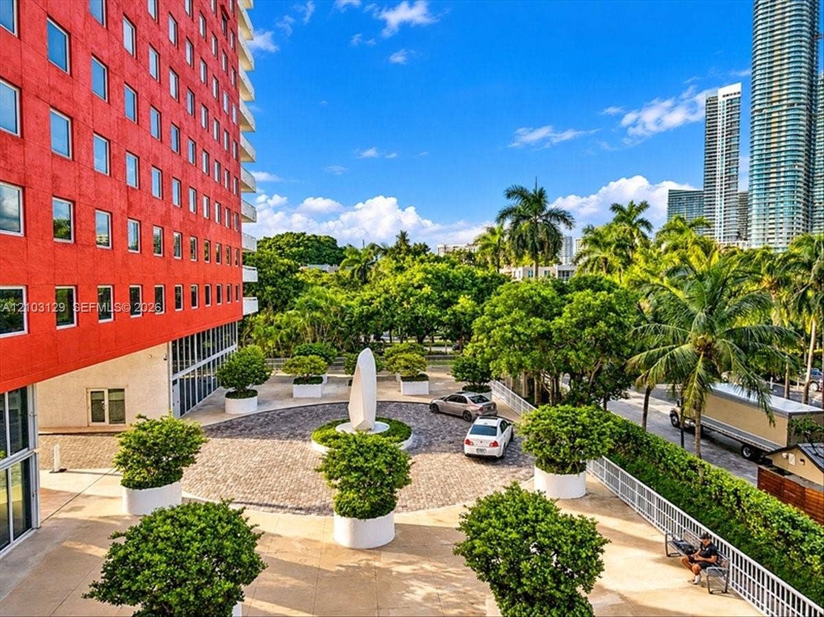 1627 Brickell Avenue, #2005, Miami, FL 33129 High-rise exterior featuring vibrant red concrete facade, circular cobblestone motor court, central sculptural focal point, and landscaped planters with integrated greenery