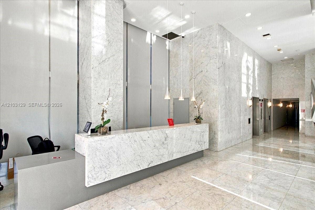 1627 Brickell Avenue, #2005, Miami, FL 33129 High-ceilinged lobby featuring full-height stone wall cladding, polished stone flooring, a custom stone reception desk, and minimalist pendant lighting