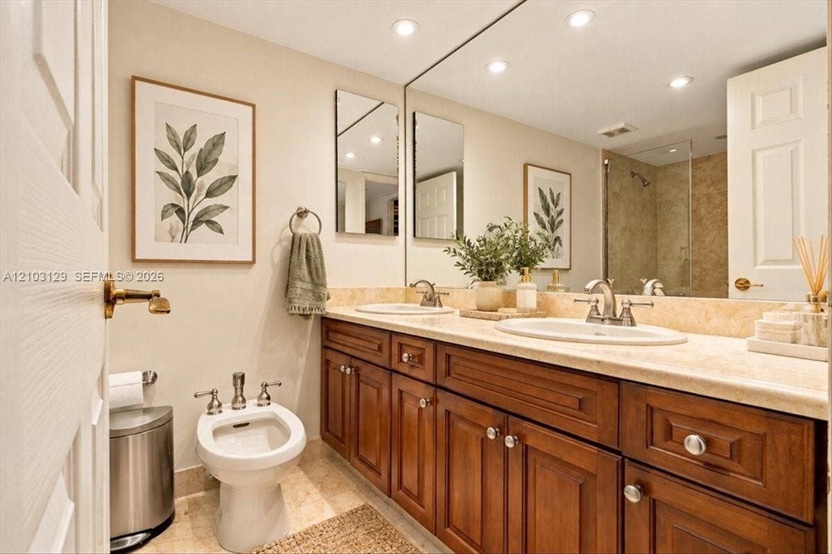 1627 Brickell Avenue, #2005, Miami, FL 33129 Double vanity with stone countertop, undermount sinks, wood-finish cabinetry, full-width wall mirror, and porcelain bidet