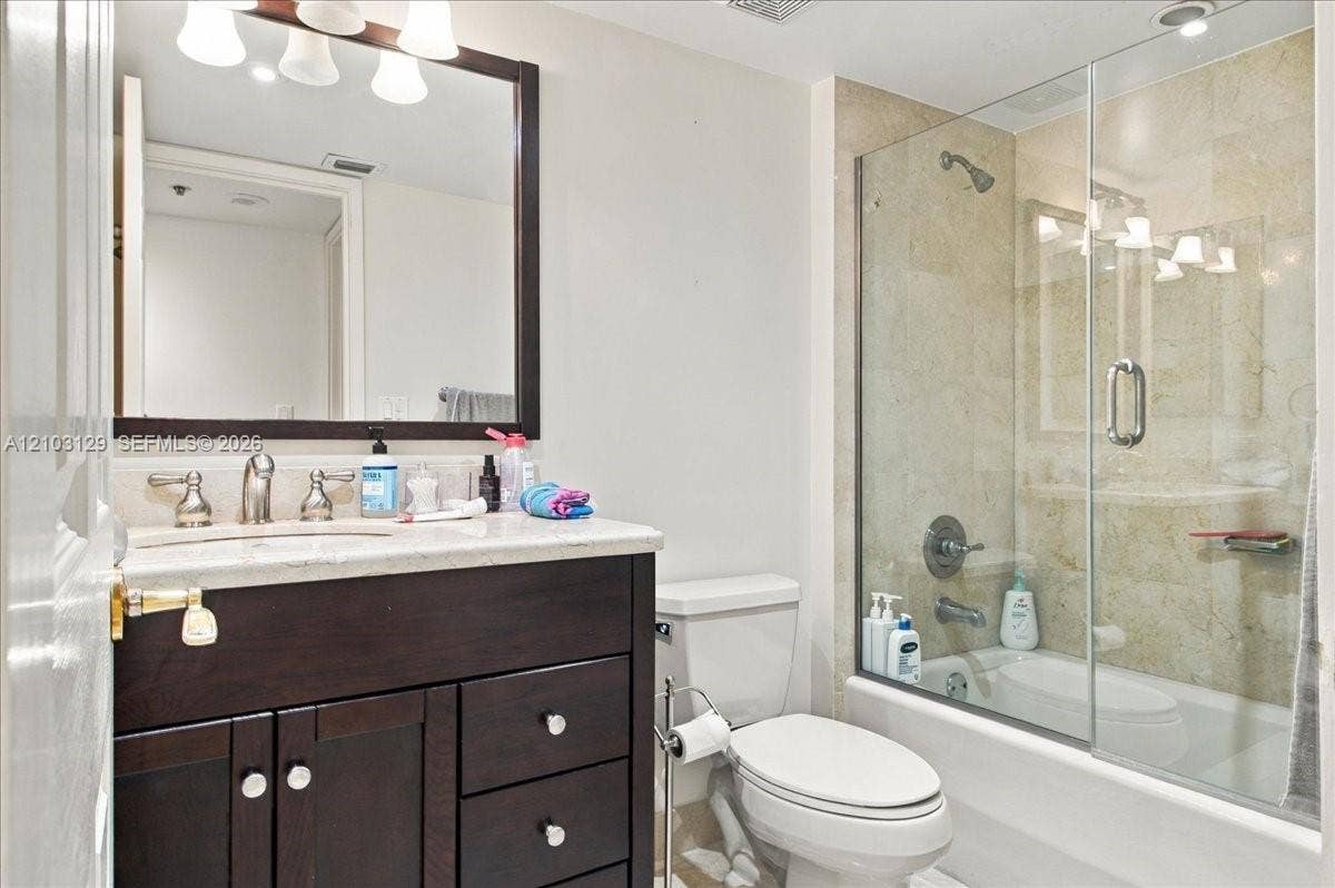 1627 Brickell Avenue, #2005, Miami, FL 33129 Dark-finish wood cabinetry, stone-surface countertop, rectangular undermount sink, framed wall mirror, and tub-shower combination featuring a glass enclosure and stone-tile surround