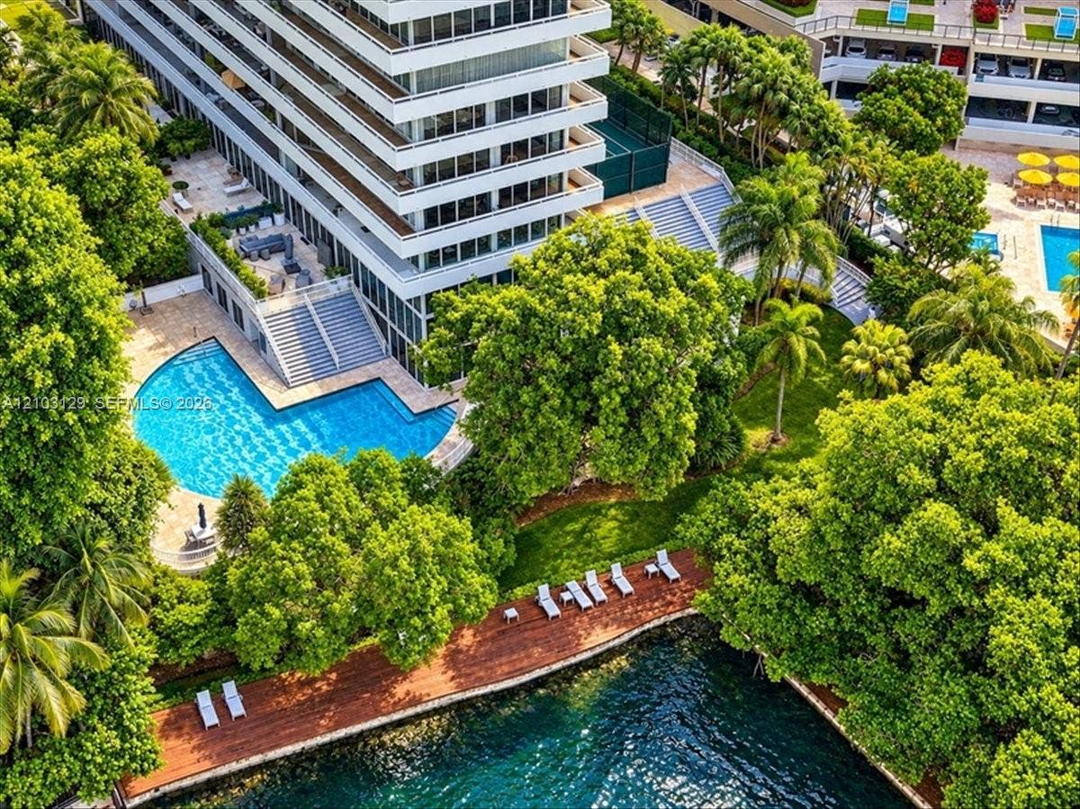 1627 Brickell Avenue, #2005, Miami, FL 33129 High-rise building exterior featuring tiered balconies, a sprawling swimming pool with surrounding terrace, a private tennis court, and a wood-decked shoreline