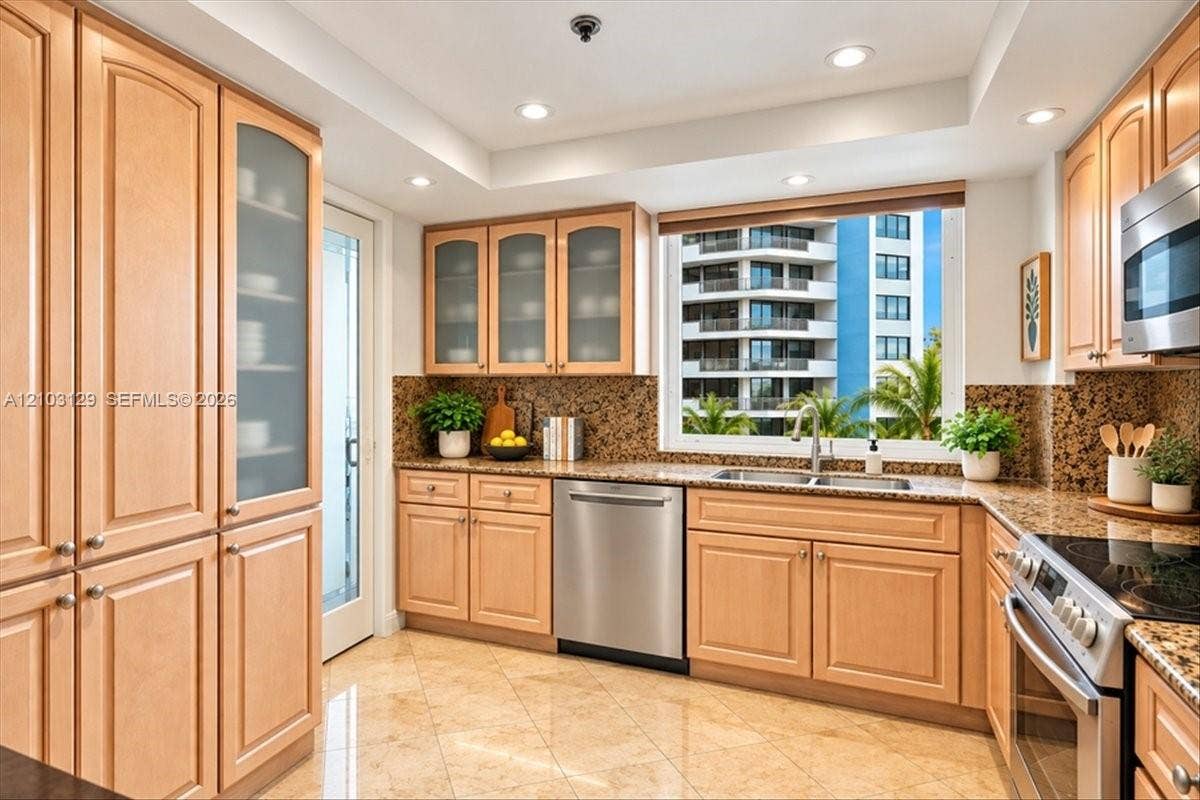 1627 Brickell Avenue, #2005, Miami, FL 33129 Kitchen featuring light wood cabinetry with glass-front uppers, stone countertops and backsplash, tile flooring, recessed lighting, and stainless steel appliances