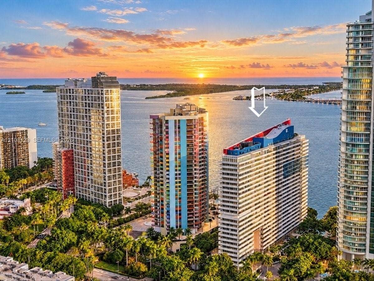 1627 Brickell Avenue, #2005, Miami, FL 33129 High-rise residential building featuring expansive coastal water frontage, architectural rooftop detailing, and surrounding mature tropical landscaping