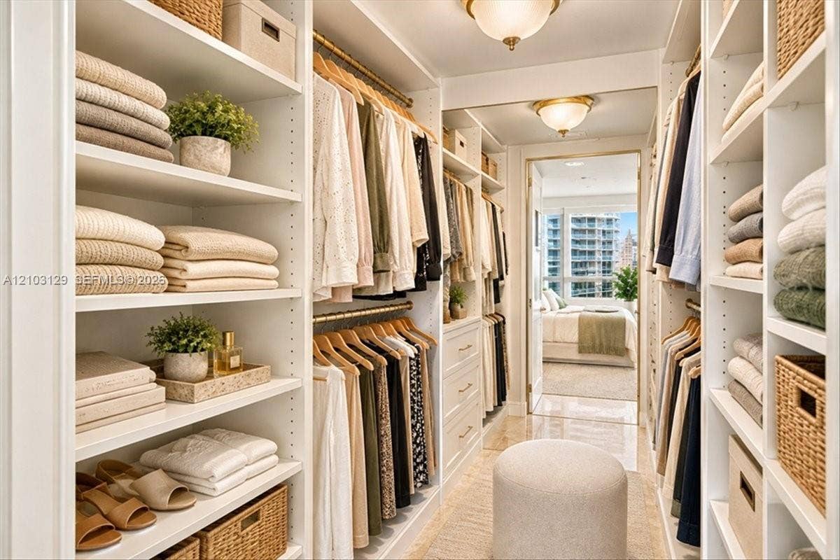 1627 Brickell Avenue, #2005, Miami, FL 33129 Custom walk-in closet featuring extensive built-in white shelving, integrated hanging rods, recessed drawer storage, and two flush-mount ceiling light fixtures