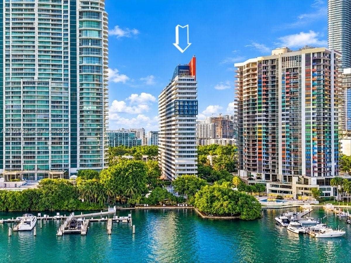1627 Brickell Avenue, #2005, Miami, FL 33129 High-rise residential building featuring expansive glass paneling, a distinctive architectural roofline, white exterior facade, and direct water frontage